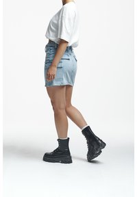 Person wearing a white oversized t-shirt, light blue denim skirt with cargo pockets, and black chunky lace-up boots walking.