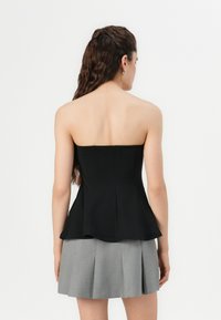 Top peplum nero senza spalline con corpetto aderente, tessuto liscio e orlo svasato. Indossato con una mini gonna plissettata grigia.