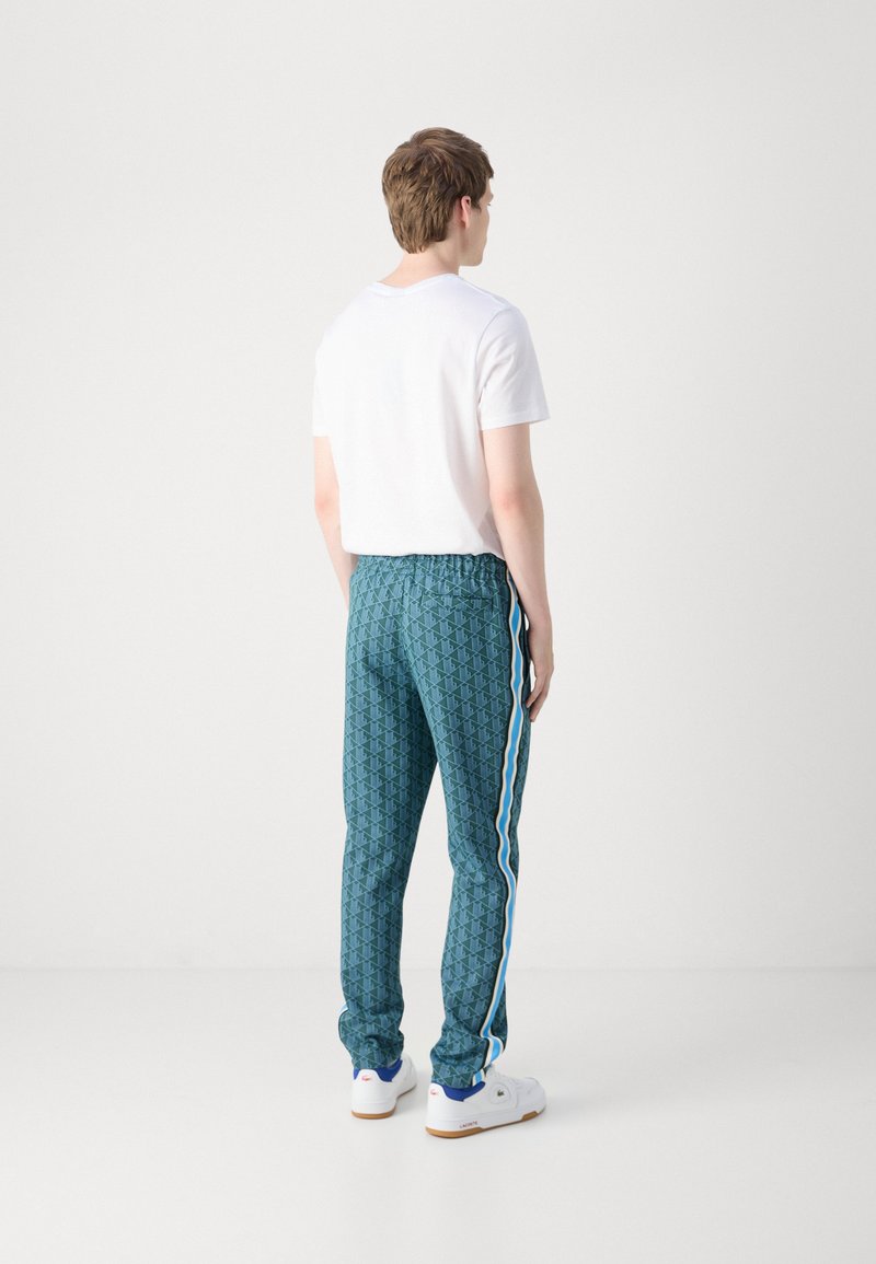 Jogging turquoise à motifs avec une taille élastique et des bandes latérales, associés à un t-shirt blanc uni et des baskets blanches.