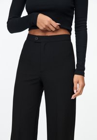 Zwarte op maat gemaakte broek van een gladde stof, met een knoopsluiting en zijzakken, in een recht model.