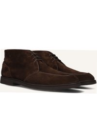 Bruine suede chukka laarzen met een ronde neus, vetersluiting aan de voorkant en een lage, donkere rubberen zool. Gladde textuur met minimale stikdetails.