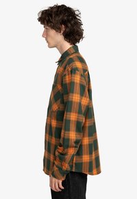 Grøn- og orangeternet flannel-skjorte, der har en afslappet pasform, lange ærmer, knap-ned krave og blød tekstur.