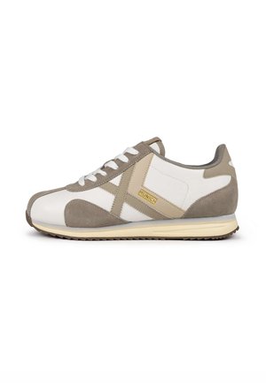 Scarpa sportiva bianca con accenti in suede grigio chiaro, design con lacci, un distintivo motivo a croce e un logo giallo "Munich" sul lato.