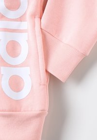 Ljusrosa sweatshirt med vit logga, med en mjuk textur, ribbade ärmslut och en sidficka för funktionalitet.