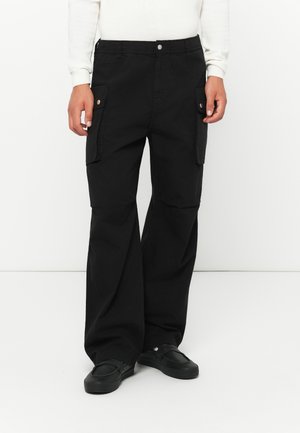 Black cargo pants with a relaxed fit, featuring two side pockets, elastic waistband, and button closure. Fabric appears sturdy and textured.