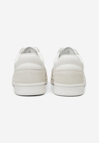 White leather sneakers with suede accents, rounded shape, minimal design, and distinct textured heel. Laced closure, rubber sole.