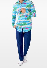 Camicia colorata a maniche corte con sfondo turchese, fenicotteri rosa, palme verdi e strisce blu, abbinata a pantaloni navy.