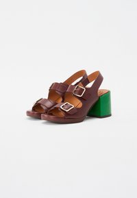 Sandalias de plataforma de cuero burdeos con dos correas ajustables y hebillas plateadas; el tacón verde añade un elemento de contraste.