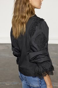 Black long-sleeve blouse with puffed sleeves, featuring intricate lace accents on shoulders and hem, worn over blue jeans.