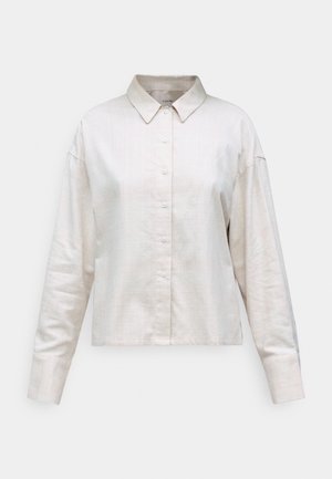 Light beige collared shirt made from textured fabric with a button front and long sleeves, featuring a cropped design and relaxed fit.