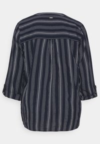 Chemise bleu marine à rayures blanches verticales et horizontales, manches longues retroussées et petite étiquette dans le haut du dos.