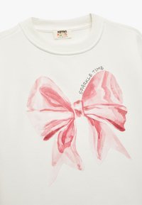 Witte sweater met een groot roze aquarel strikontwerp en de tekst "SPARKLE TIME" in het zwart boven de strik. Zachte textuur.