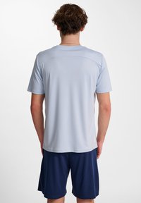 Ljusblå, fukttransporterande träningsskjorta med korta ärmar, med rundad hals och en slät yta, kombinerad med marinblå shorts.