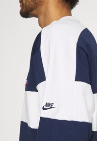 Marinblå och vit randig sweatshirt i en bomullsblandning med broderad logotyp på ärmen och flerfärgad etikett på axeln.