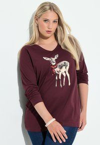 Viininpunainen pitkähiha T-paita, jossa on hertta graafinen kuva punaisella paljettilipulla. Pehmeä kangas ja V-kaula-aukko. Yhdistetty sinisiin farkkuihin.