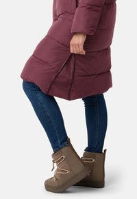 Mørkerød pufferjakke med lynlåslukket sideslids, parret med mørkeblå jeans og brune ankelstøvler med snøre detaljer og en tekstureret sål.