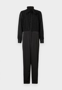 Combinaison noire avec un haut texturé et scintillant, col montant avec un nœud, et un bas lisse et ajusté, manches longues et jambes fuselées.