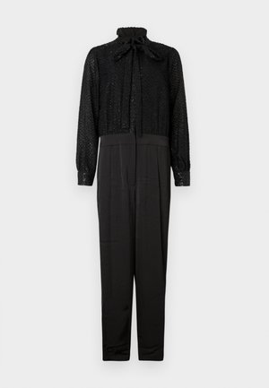 Zwarte jumpsuit met een gestructureerde, glinsterende top met een hoge hals en strik, en een glad, aansluitend broekgedeelte met lange mouwen en taps toelopende pijpen.