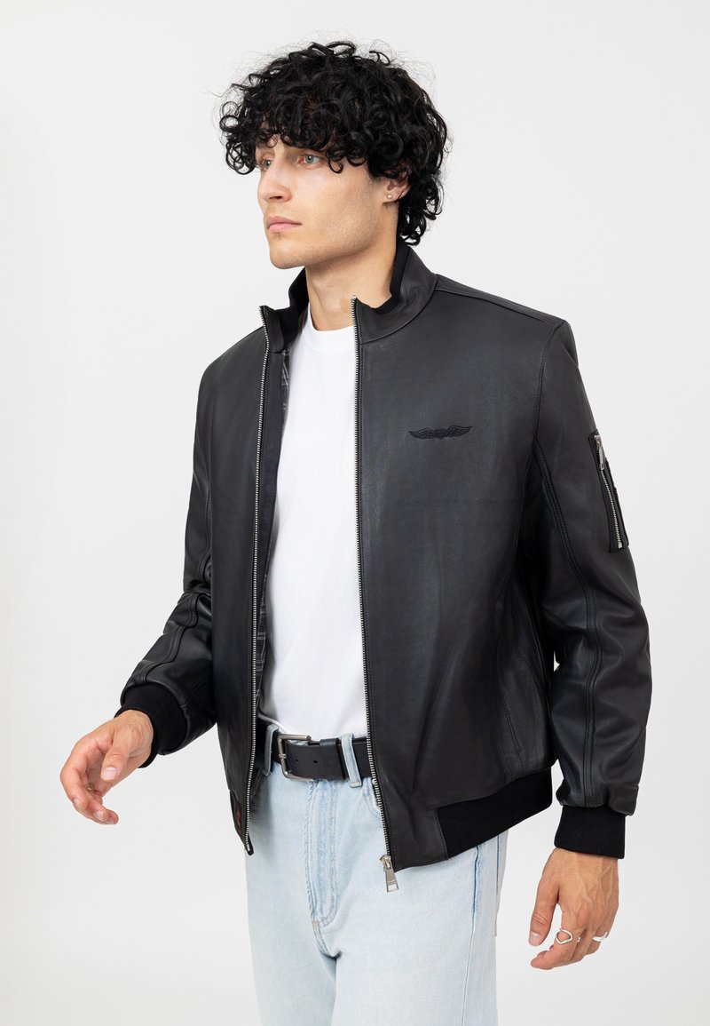 Giubbotto bomber in pelle nera con colletto alto, chiusura con zip e polsi a costine. Presenta un piccolo dettaglio del logo sul petto e una tasca laterale.