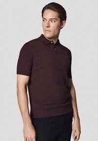 Koszulka polo z krótkim rękawem w ciemnym burgundowym dzianinowym materiale. Posiada klasyczny kołnierzyk, zapięcie na trzy guziki oraz slim fit. Minimalistyczny design.