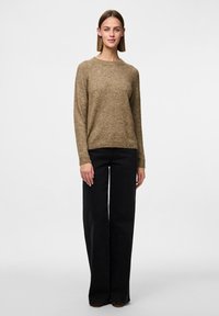 Maglione di lana marrone con scollatura rotonda e maniche lunghe, abbinato a jeans neri a vita alta e gamba larga; design semplice e testurizzato.