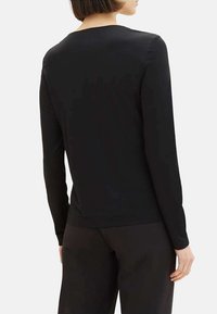 T-shirt noir à manches longues en tissu doux, avec un col rond simple et une texture lisse, ajusté à la taille.