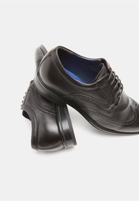 Zapatos de vestir de cuero negro con diseño tipo wingtip, punta redonda y perforaciones decorativas. Cuentan con un acabado suave y suela de goma texturizada.