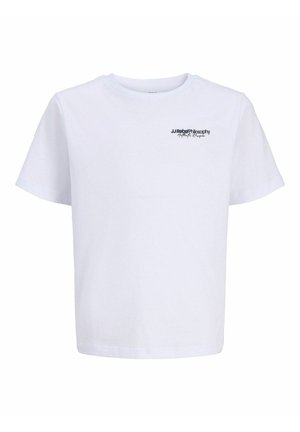 Garçon debout, portant un t-shirt blanc à manches courtes, un pantalon cargo noir et des baskets blanches, regardant vers sa gauche sur un fond blanc uni.