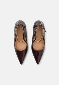 Burgunder patentlæder pumps med spids tå, ankelrem og åbne sider. Tekstureret indvendig med brandlogo synligt på sålen.