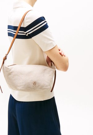 Bolso de lona a rayas con correa de cuero marrón y herrajes dorados, con un detalle de monograma en la parte frontal.