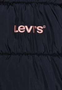 Levi's logo izvezena ružičastim koncem na tamnoplavoj kviltanoj tkanini s horizontalnim šavovima.