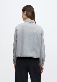 Szürke farmerdzseki rövidített kialakítással, gombos mandzsettákkal és klasszikus gallérral. Sima textúra és visszafogott varrási részletek.