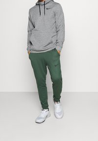 Harmaa huppari mustilla yksityiskohdilla, vihreät collegehousut mustalla logolla ja valkoiset lenkkarit mustilla ja vihreillä yksityiskohdilla.