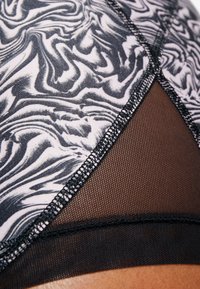 Brassiere sportivo bianco e nero con motivo marmorizzato, pannelli in rete e cuciture piatte. Tessuto testurizzato con una finitura liscia.