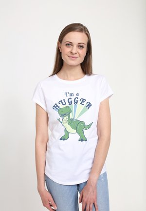 Biała koszulka z krótkim rękawem z zielonym rysunkowym dinozaurem oraz napisem "Jestem PRZYTULASEM" w niebieskim i czarnym, na neutralnym tle.