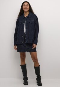 Jeans jakna in kratek temno modri krilo, okrašen z srebrnimi žebljički, z gumbi spredaj in dvema žepoma na prsih. Črne gumijaste škornje do kolen dopolnjujejo izgled.