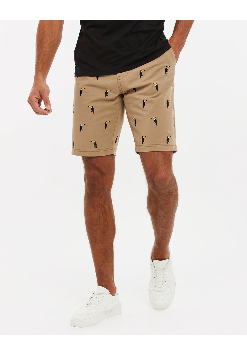 Beige Shorts mit einem sich wiederholenden schwarzen Tukanmuster, aus leichtem Material mit geradem Schnitt und seitlichen Taschen.