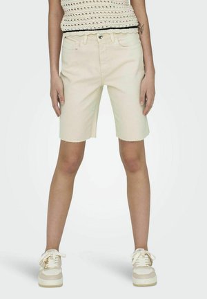 Shorts de denim beige claro con un dobladillo deshilachado, cinco bolsillos y un cierre delantero con botón, combinados con zapatillas blancas y una blusa de punto.