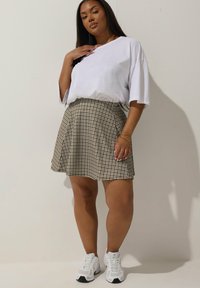 Witte korte mouwen t-shirt gecombineerd met een beige geruite geplooide rok en witte sportschoenen. Soepele stof, relaxed fit en casual stijl.