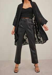 Czarna przezroczysta kimono w kwiatowy wzór, nałożona na czarny prążkowany crop top i wysokie na biodrach spodnie z faux skórki. Podkreślona wysokimi obcasami.