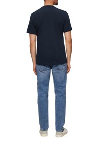 Granatowa bawełniana koszulka z okrągłym dekoltem, zestawiona z jasnymi dżinsami i białymi trampkami, widok z tyłu. Prosty design i krój.