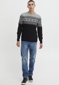 Schwarzer und grauer gemusterter Pullover mit rundem Ausschnitt, ausgestattet mit einem dekorativen Strickbereich. Getragen mit blauen Jeans und schwarzen Sneakers.