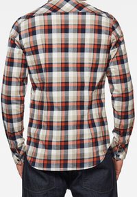 Långärmad rutmönstrad skjorta med navy, röd, beige och grå rutor; knäppbar krage; rundad nederkant; och knappade ärmslut. Tillverkad av bomull.