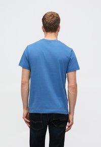 Zila kokvilnas T-kreklu ar apaļu dekoltē un īsām piedurknēm, saskaņots ar tumšiem džinsiem. Redzami šuvumi un vienkāršs dizains aizmugurē.