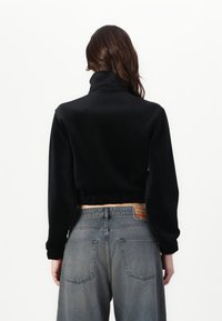 Svart cropped sweatshirt med høy krage, myk tekstur og elastisk liv, parret med falmede grå høytaljede jeans med lommer.