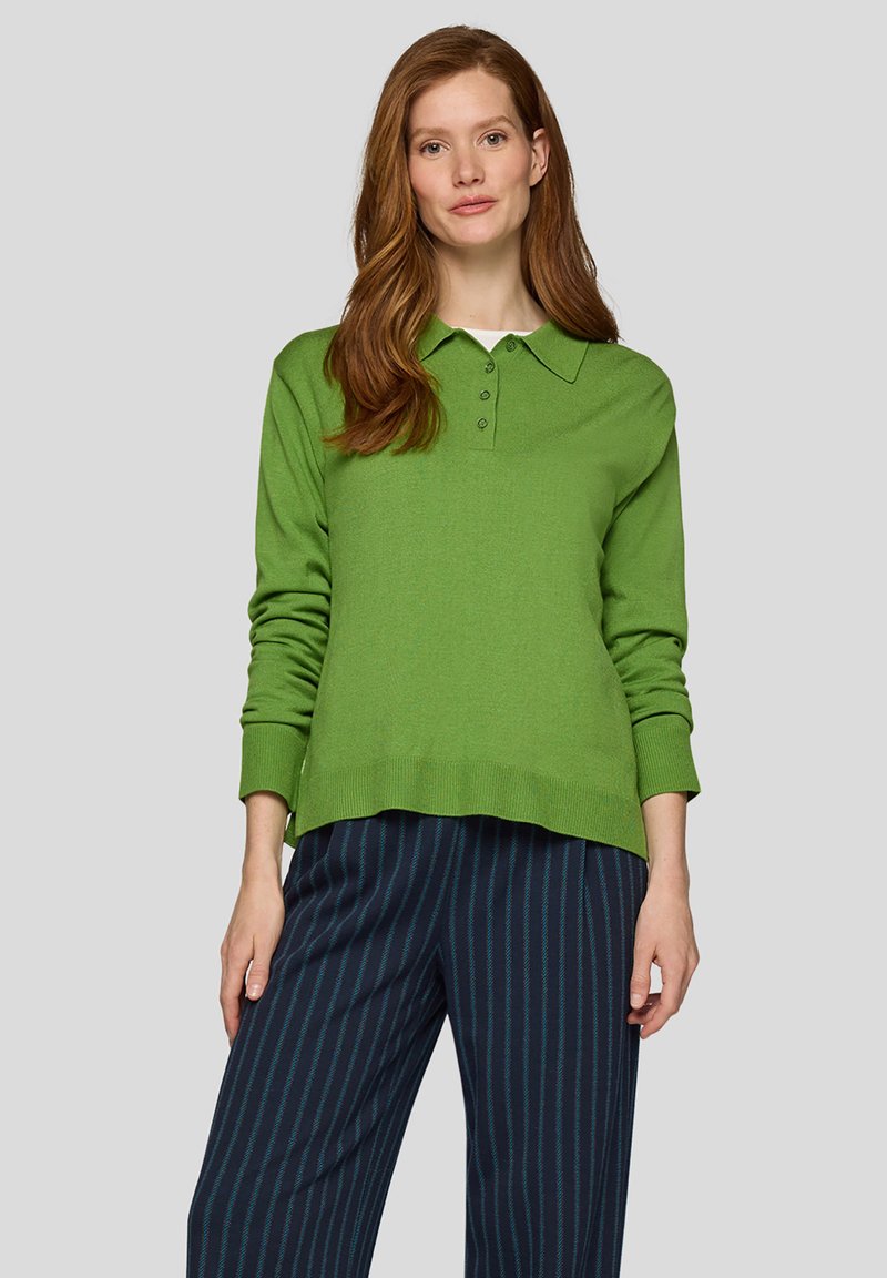 Grüner Langarm-Polo-Pullover mit Kragen, ausgestattet mit einem Knopfverschluss mit vier Knöpfen und gerippten Manschetten. Kombiniert mit marineblauen gestreiften weit geschnittenen Hosen.