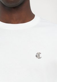 Hvit bomulls T-skjorte med rund hals, med et sølvfarget logoaksent på brystet. Glatt tekstur og klassisk passform.