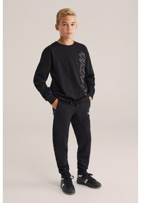 Schwarzes Langarmshirt mit grauem Logo-Print; kombiniert mit schwarzen Jogginghosen. Das Outfit zeichnet sich durch eine bequeme Passform und strapazierfähiges Baumwollmaterial aus.