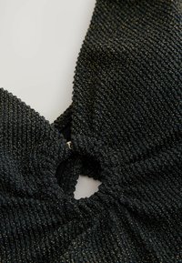 Haut en tissu noir texturé avec un centre serré froncé et des éclats dorés. Présente une ouverture circulaire au centre et un design de cou halter.