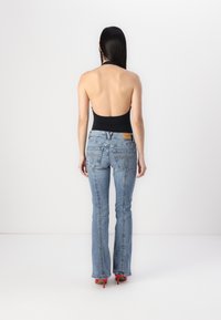 Fekete hát nélküli bodynadrág világoskék, bő szárú farmernadrággal, amely varrott részletekkel és zsebekkel rendelkezik, piros magassarkú cipővel viselve.